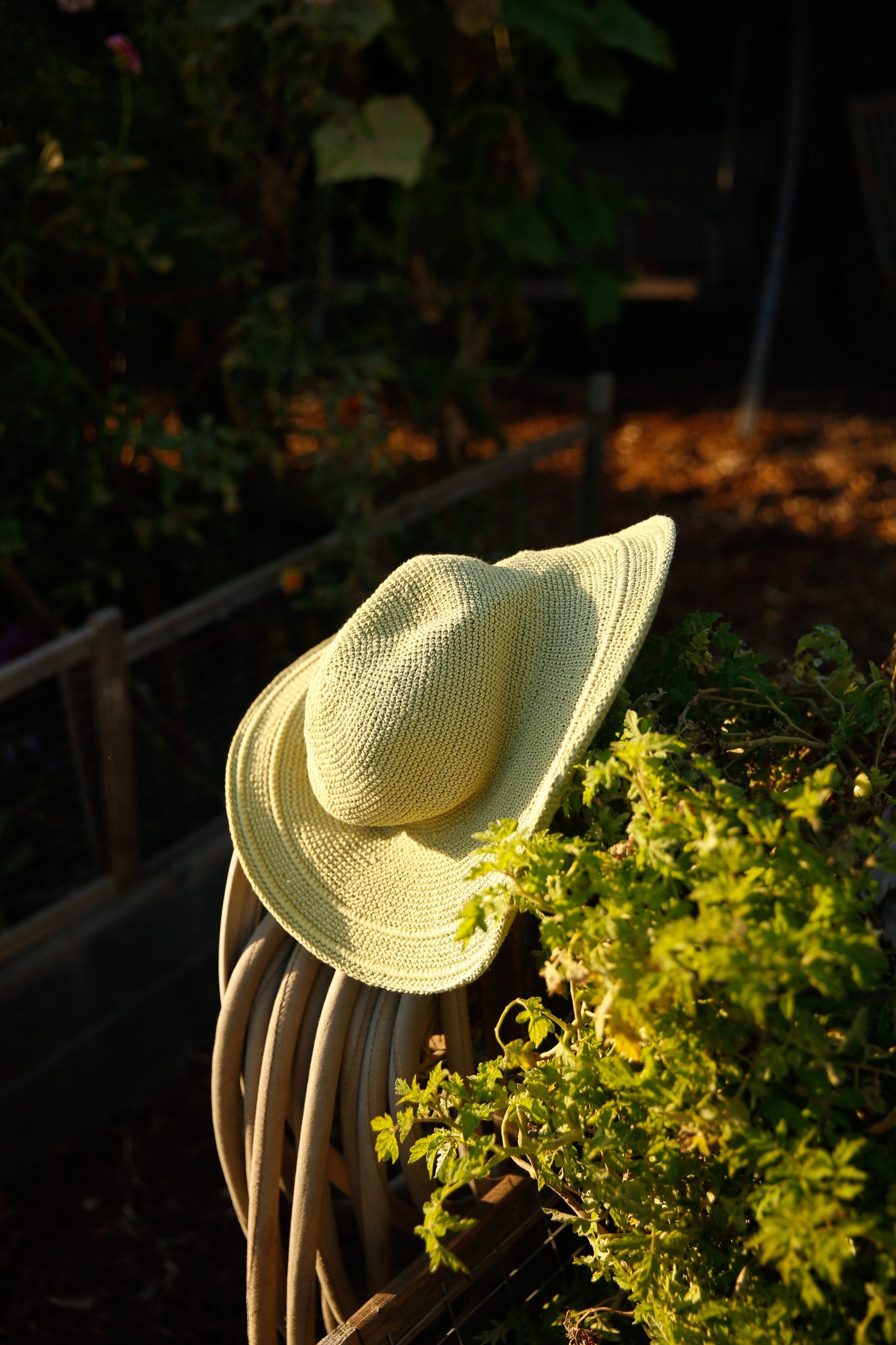 bali wide-brim hat resting on garden tools surrounded by vibrant greenery and sunlight. Crocheted sunhat handmade in Bali.