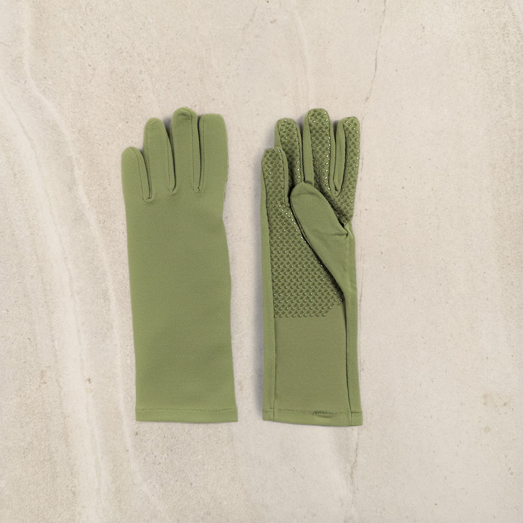 A pair of olive green gloves laid flat on a light beige textured surface. One glove is shown from the back with smooth fabric, and the other is shown from the front with textured grip panels on the back of the fingers and palm.