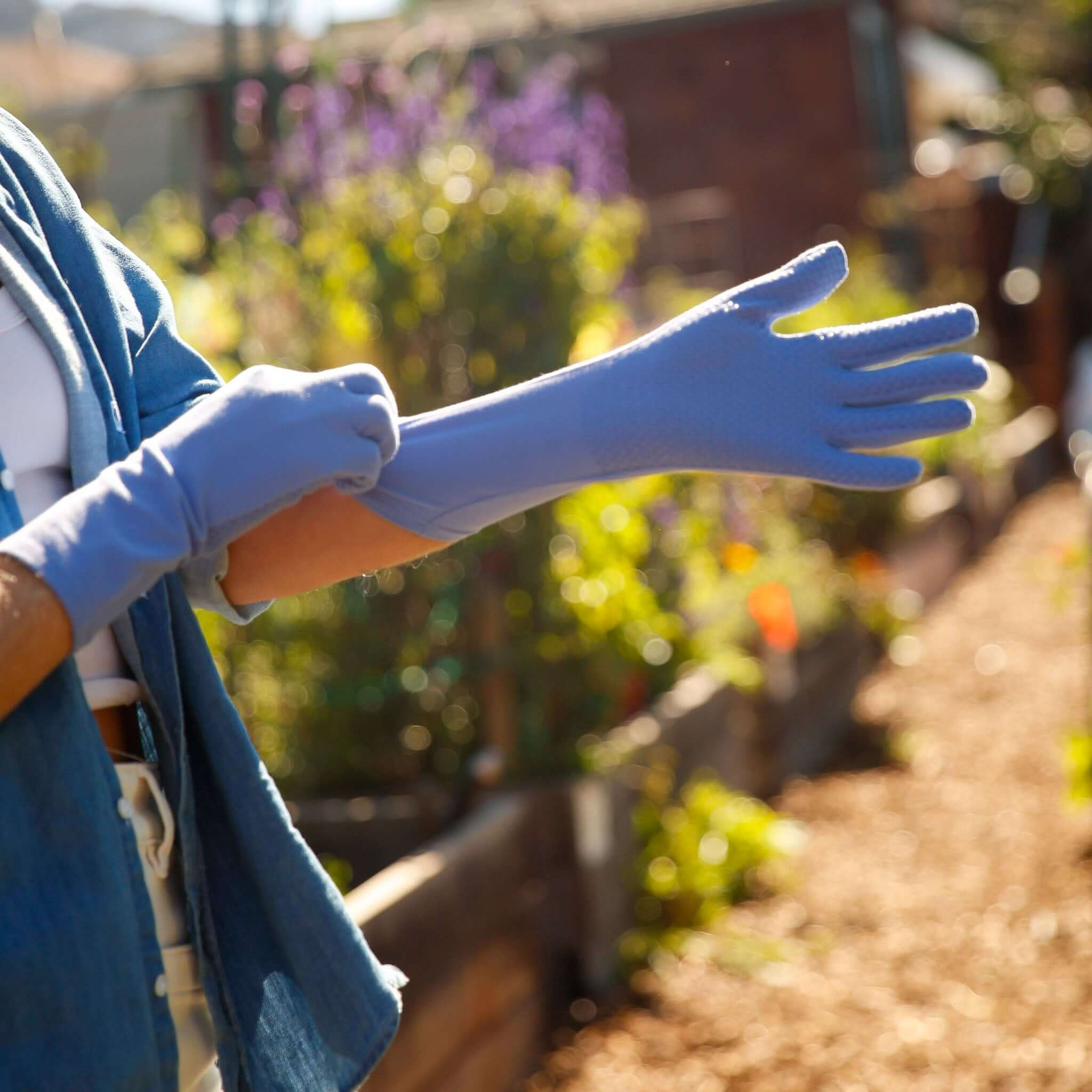 Person wearing blue gardening gloves in a garden setting