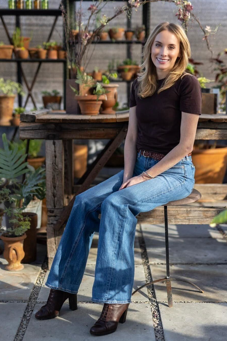 woman sits on stool in a greenhouse