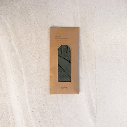 A rectangular kraft paper package with a cutout window displaying a dark olive green knit fabric item, photographed from above on a light textured surface.