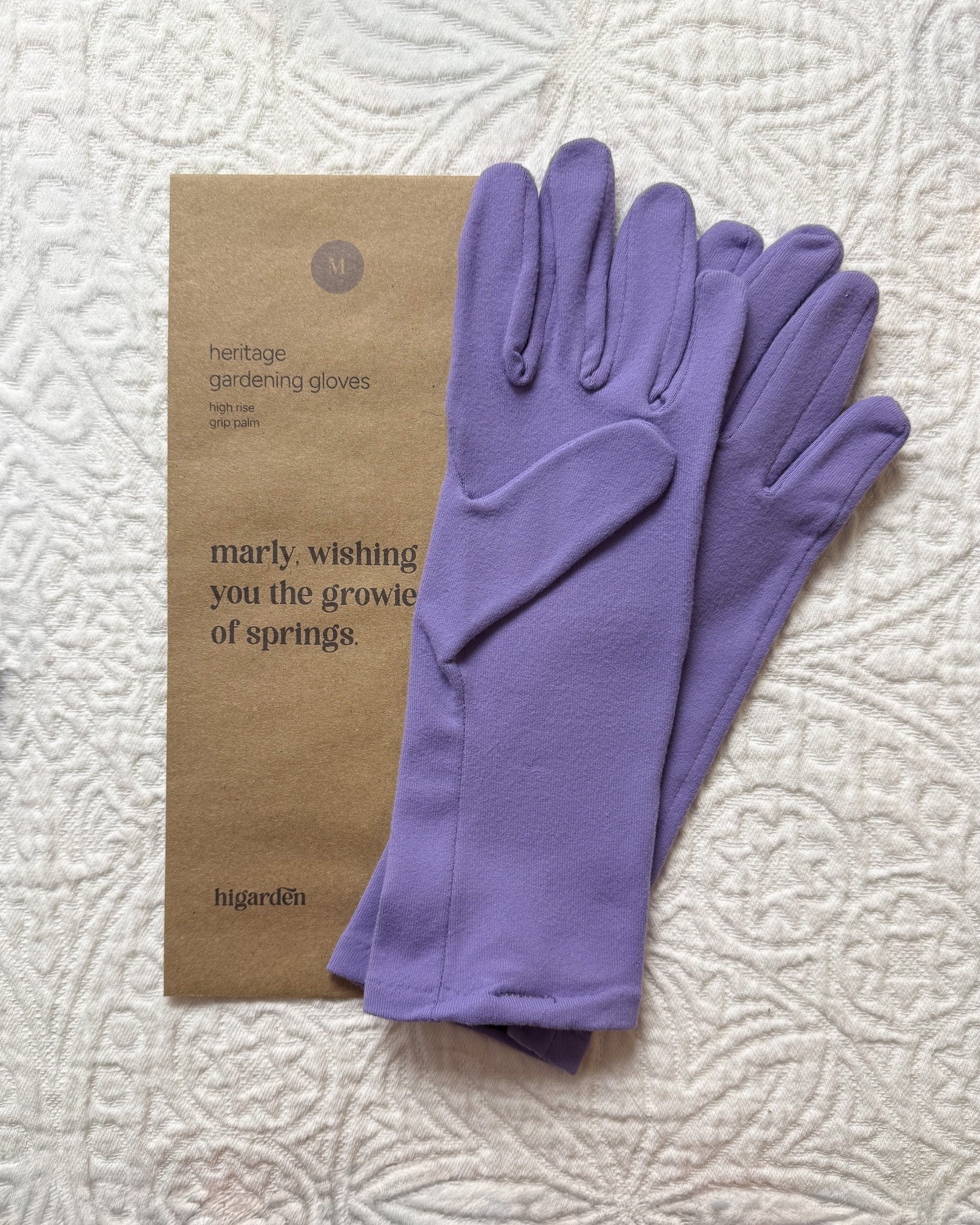 Purple gardening gloves with a branded gift box on a textured white background