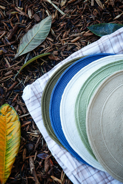 Bali wide-brim hat collection in various colors on plaid fabric surrounded by natural mulch and leaves. Blue, white, olive green, light green sun hat. Crocheted sunhat handmade in Bali.