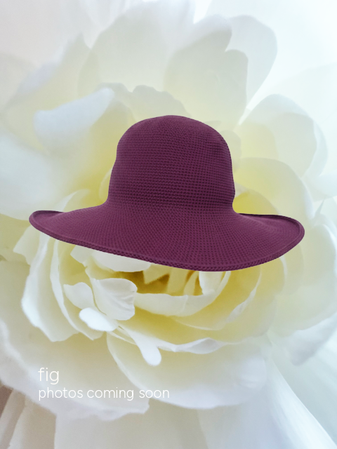 A small structured sun hat in deep plum purple, styled on top of a large white flower. Text in the bottom-left corner reads 'fig photos coming soon'.