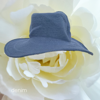 A small denim sun hat in a dusty blue-gray color, styled on top of a large white flower.