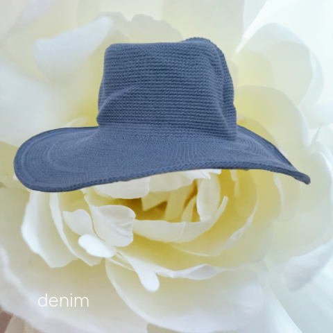 A small denim sun hat in a dusty blue-gray color, styled on top of a large white flower.