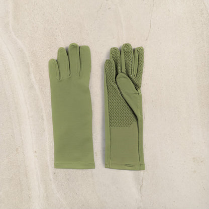 A pair of olive green gloves laid flat on a light beige textured surface. One glove is shown from the back with smooth fabric, and the other is shown from the front with textured grip panels on the back of the fingers and palm.
