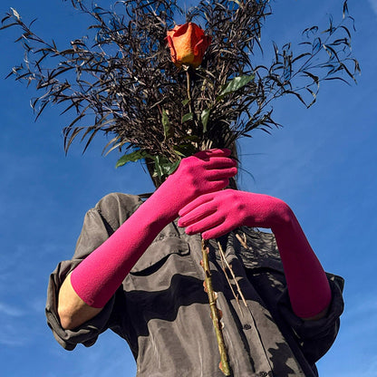 Person wearing pink gloves holding a bundle of sticks with a red rose against a blue sky.